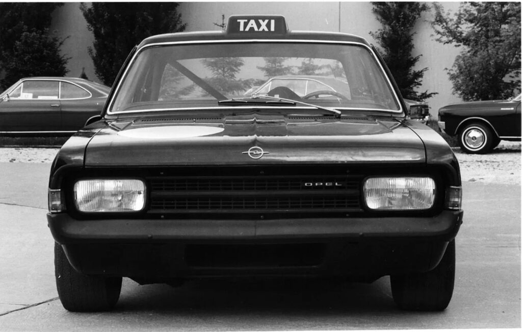 Als der Rekord C erschien, war die Taxi-Farbe in Deutschland noch Schwarz. So montierten die Opel-Designer als Gag der „Schwarzen Witwe“ auch einmal ein Taxi-Schild. Im Hintergrund ist das neue Opel Rekord C Coupé zu sehen.
